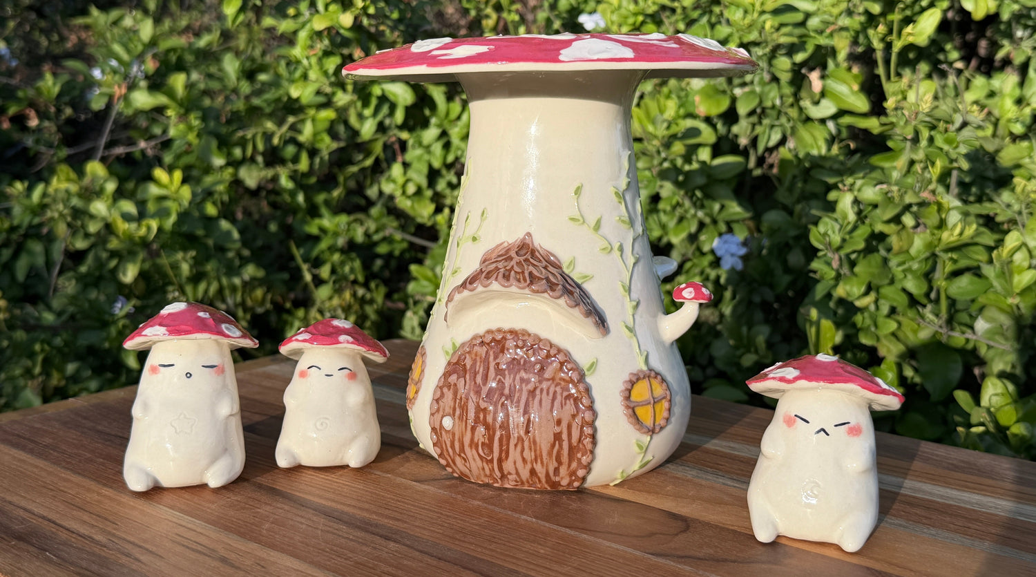 Ceramic mushroom-shaped figures with a small house-like structure on a wooden surface with a green outdoor background.